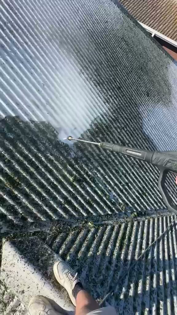 High-pressure surface cleaning removing moss and grime from corrugated metal roof